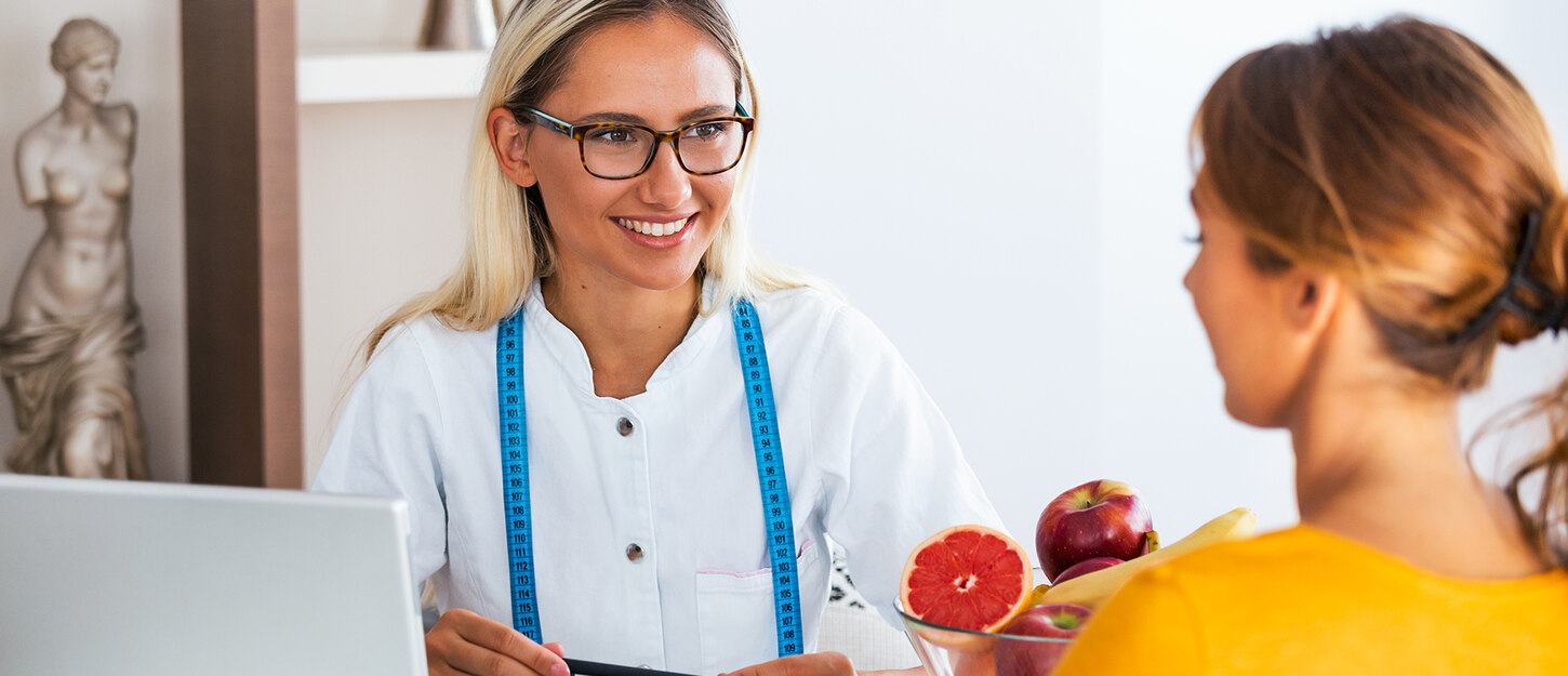 Diätassistentin berät eine junge Frau. Neben ihr liegt frisches Obst